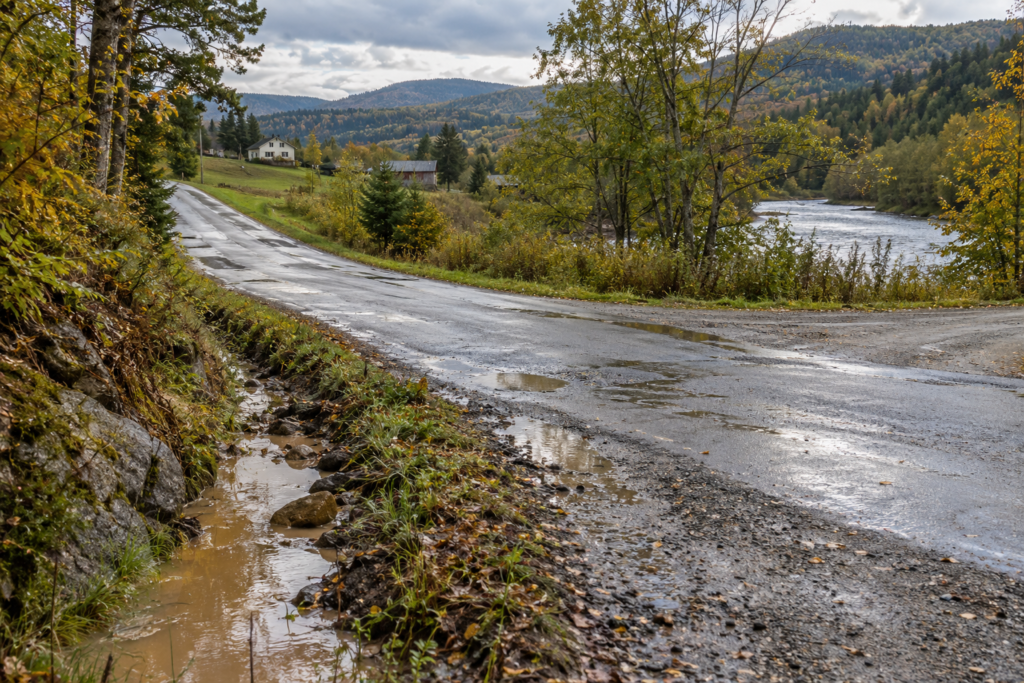 AI-generated view of runoff at a fictional Alder Valley road junction after rain; no cause or engineering solution is established.