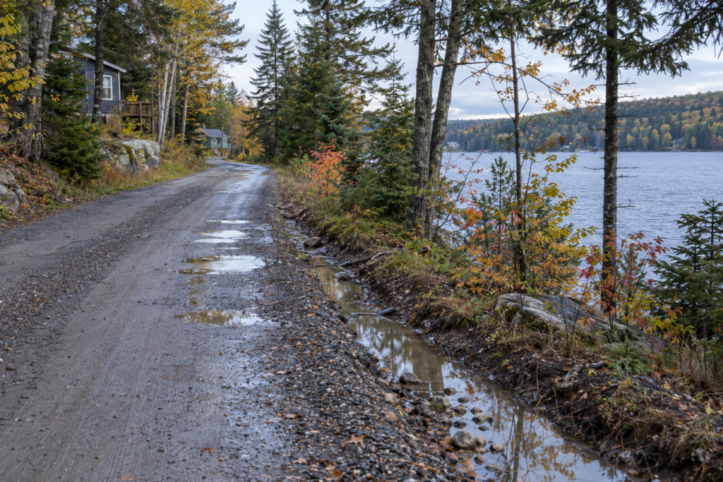 AI-generated view of the narrow fictional Pinehaven lakeside road after rain; no repairs or widening have been approved.